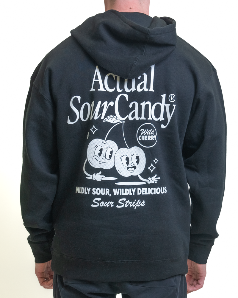 The person is wearing a black Retro Cherry Hoodie by SourStrips, featuring an oversized fit and unisex design. It has white text and graphics on the back with two cartoon cherries, saying "Actual Sour Candy, Wild Cherry, Wildly Sour, Wildly Delicious".