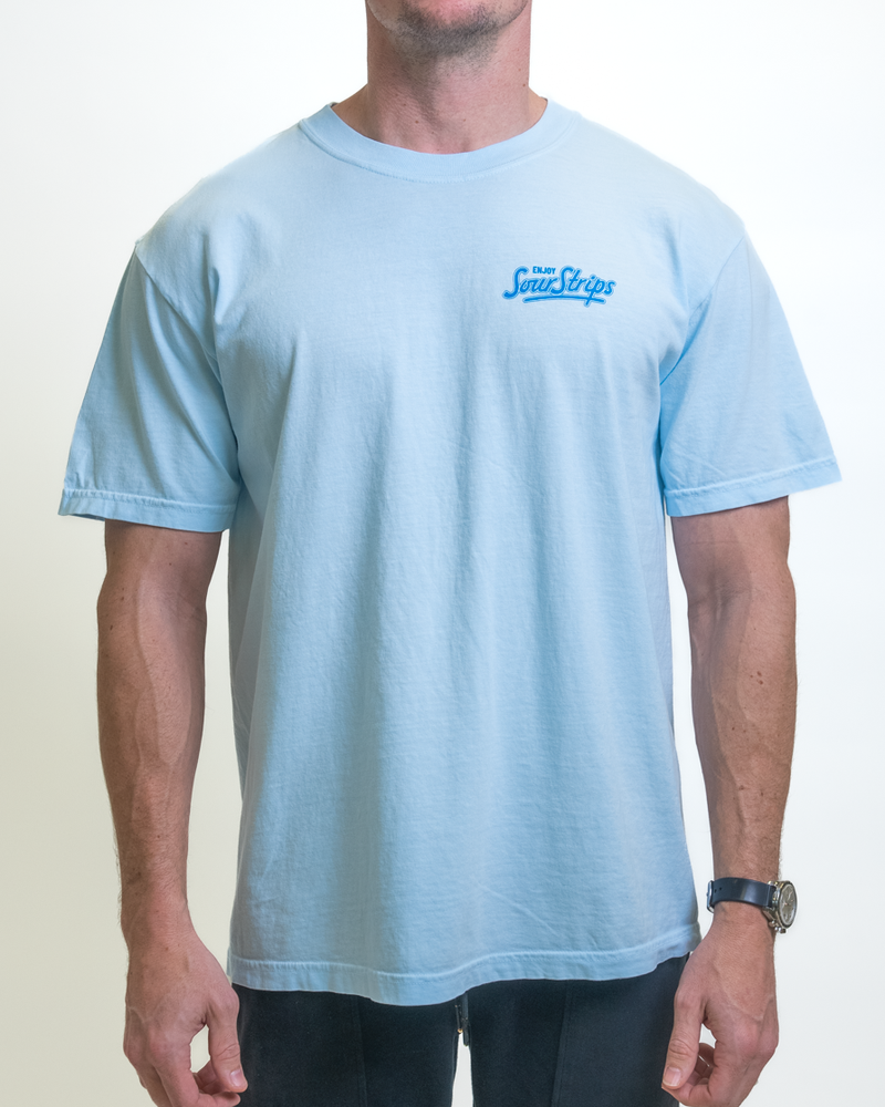 A person is sporting a Retro Blue Raspberry Tee by SourStrips featuring a small "Snow Socks" logo on the chest. Its oversized box fit adds trendiness. They're wearing a watch on their left wrist and standing against a plain white background, showcasing the relaxed vibe of SourStrips apparel.