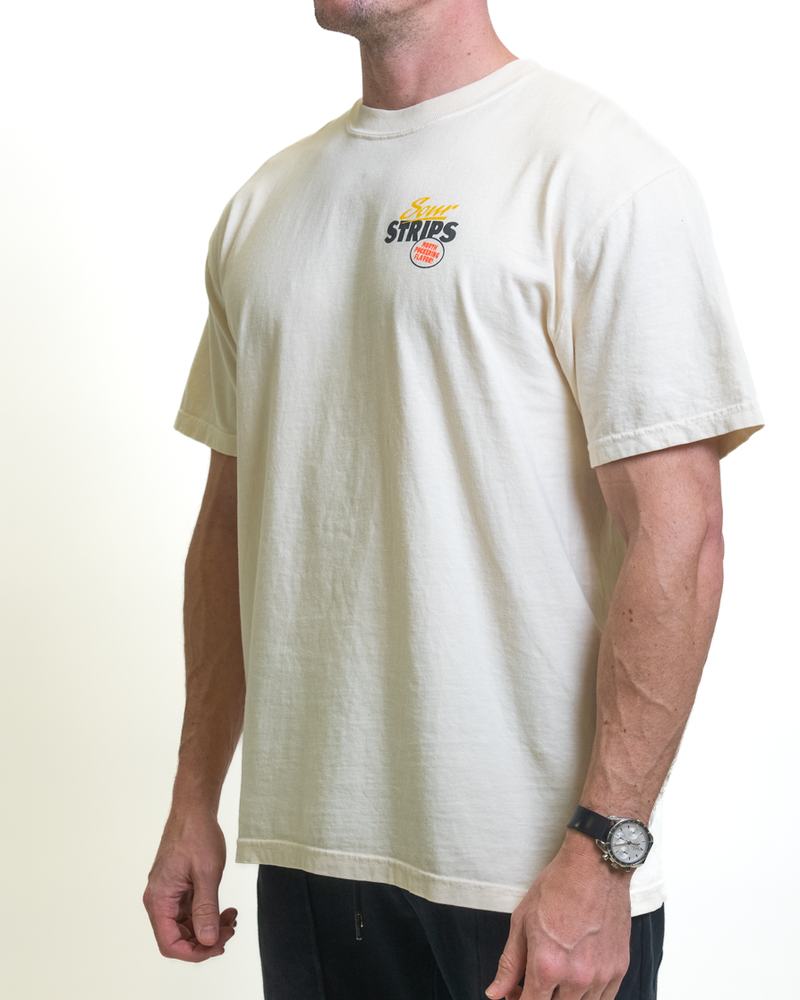 A man in an oversized Retro Watermelon Tee by SourStrips, with "Super Strips" and a small orange logo, stands against a white backdrop. Dark pants and a wristwatch complete his look, making the unisex graphic T-shirt stand out.