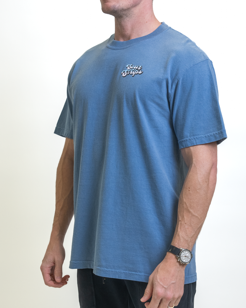 A person is wearing an oversized blue SourStrips Retro Strawberry Tee with "Salty Dogs" on the chest. The unisex design complements the watch on their left wrist, set against a plain white background.