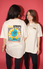 Two people flaunt oversized Retro Watermelon Tees from SourStrips with colorful graphics on the back. One faces away, showing "Sour Strips" and "Actual Sour Candy," while the other smiles. These unisex cotton shirts stand out against a vibrant pink background.