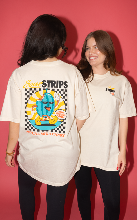 Two people flaunt oversized Retro Watermelon Tees from SourStrips with colorful graphics on the back. One faces away, showing "Sour Strips" and "Actual Sour Candy," while the other smiles. These unisex cotton shirts stand out against a vibrant pink background.