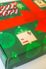 The SourStrips Holiday Gift Box-Fourteen Pack features green packaging with red ribbon, snowflakes, and trees, plus a fun Santa gift tag—perfect for gifting Sour Strips and exclusive limited edition stickers.