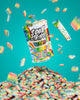 A colorful package of Sour Strips Bites is shown with vibrant rainbow-colored candy pieces. Some candies are floating around the package against a bright teal background, while many more are piled below, creating an eye-catching and lively scene.