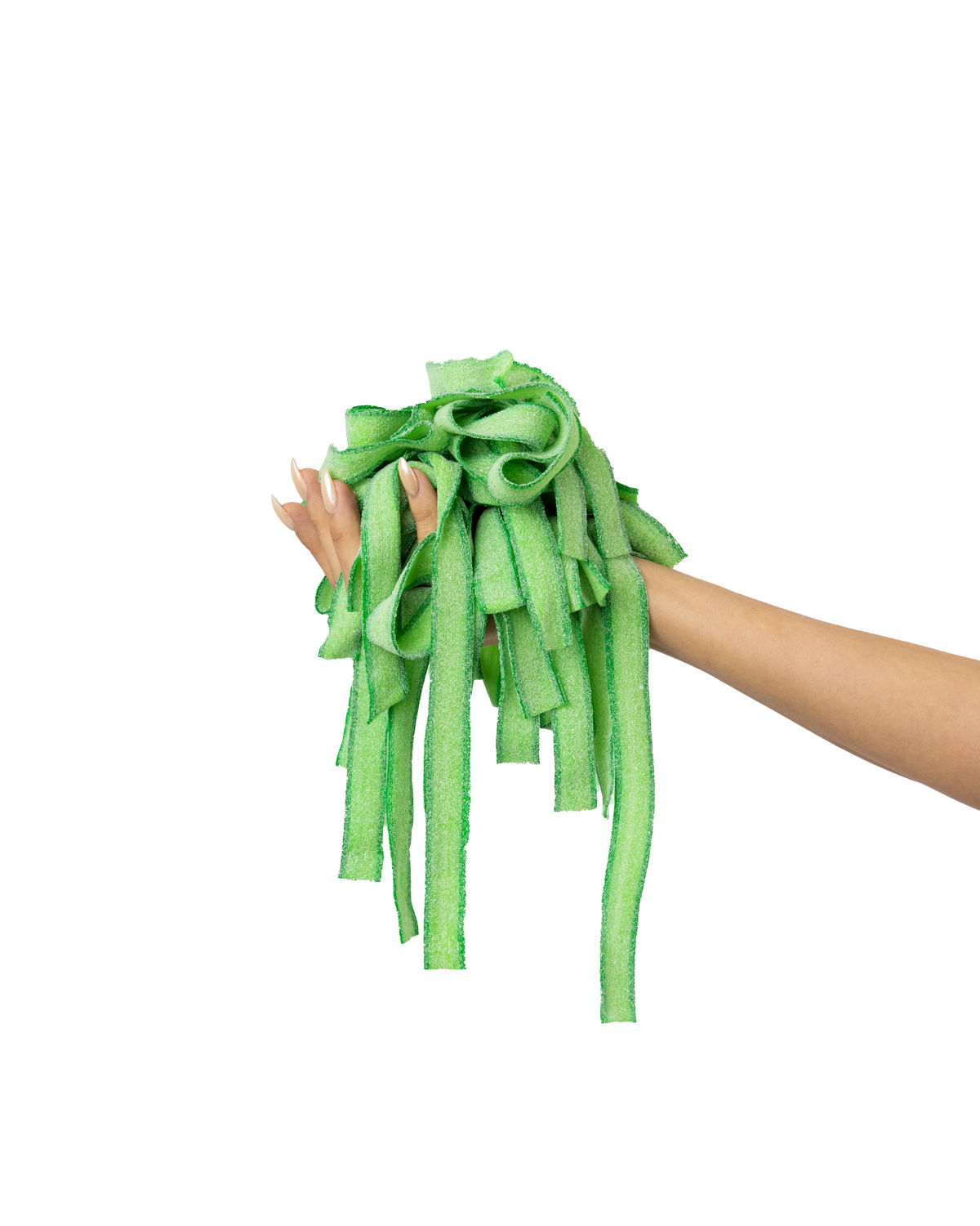 A person's hand with long manicured nails holds a bunch of green sour candy strips against a solid light green background.
