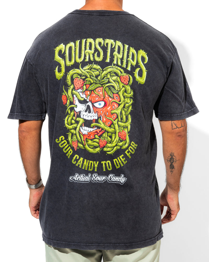 A person wearing the SourStrips Twisted Temptation Tee, a black unisex cotton shirt with a colorful skull, strawberries, and green vines on the back, and text reading "Sourstrips Sour Candy to Die For" and "Actual Sour Candy.