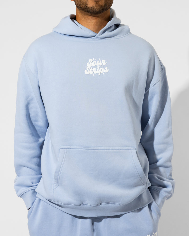 A person wearing a light blue unisex SourStrips Dreamberry Hoodie with a front pocket and "Sour Strips" in white on the chest. The person's face is partially out of frame.