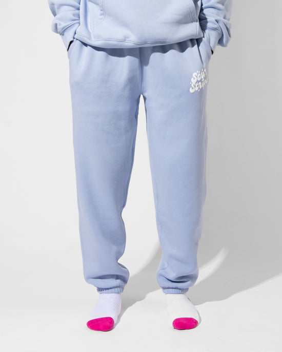 A person models SourStrips Dreamberry Joggers with a matching sweatshirt, standing on a white floor. Their lower half is shown, wearing white socks with bright pink toes.