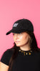 Girl wearing hat looking away. Black hat with curved brim. Sour Strips logo on front center of hat in white color. Girl is wearing gold necklace and has medium to long length dark hair.