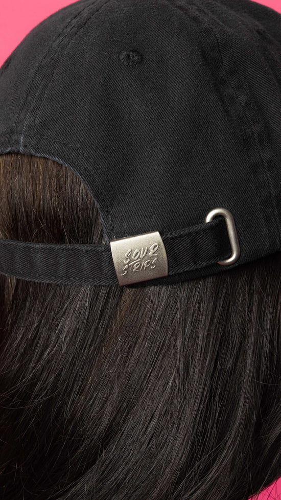 back close up of black hat on girl with dark hair. Showing details of the sour strips logo that is on the back buckle of the hat.