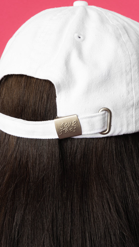 Rear of white hat. Hat is on girls head with dark hair. Close up shot is showing the sour strips logo on the back adjustment buckle.