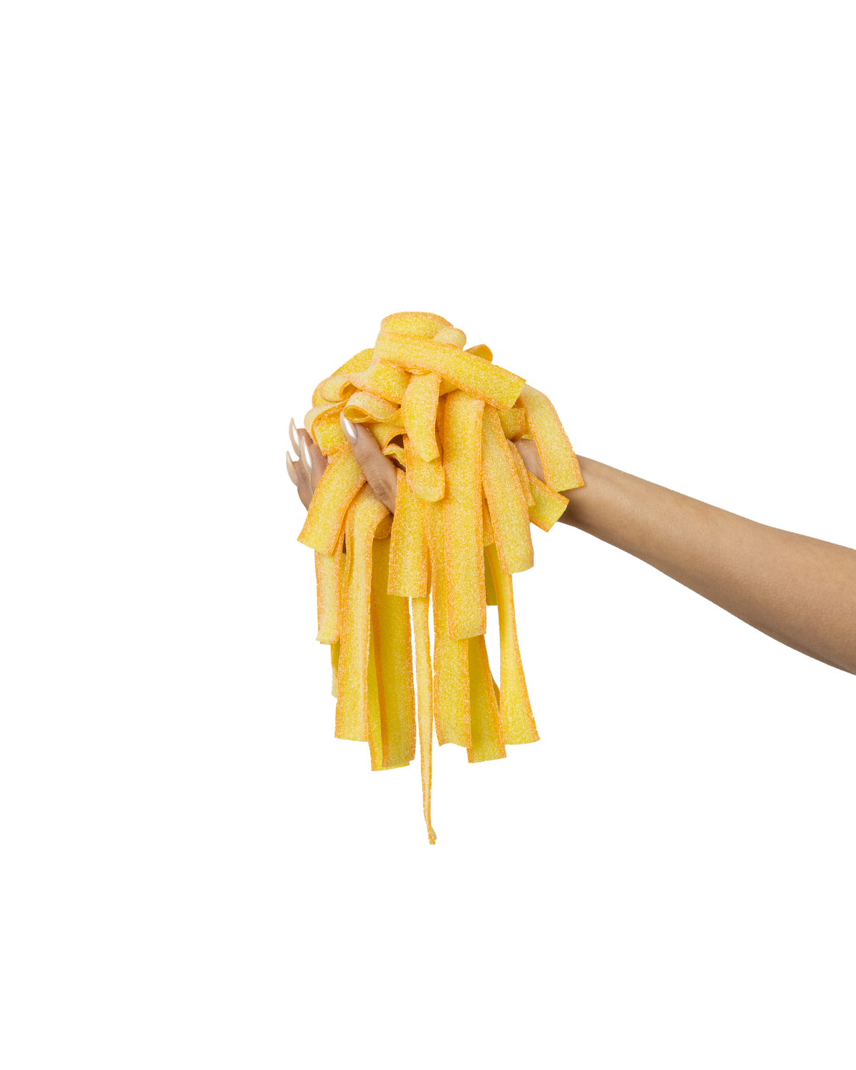 A hand with long nails holding a bunch of yellow, sugar-coated gummy candy strips against a light orange gradient background.