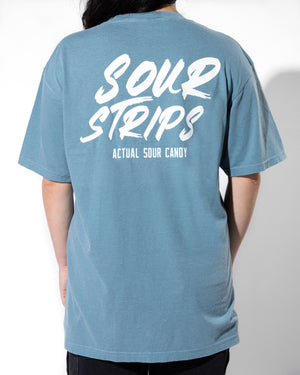 A person with long dark hair is wearing the "Logo Tee - Blue" by SourStrips, an oversized box fit graphic T-shirt. The back of the tee showcases white text with the words "SOUR STRIPS" and "ACTUAL SOUR CANDY." The unisex design is evident as the individual faces away from the camera, highlighting their back.
