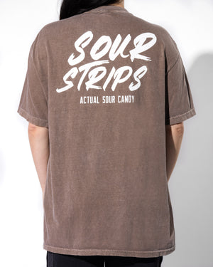A person standing with their back to the camera is showcasing a unisex design brown T-shirt. The back of the T-shirt, named "Logo Tee - Espresso" from SourStrips, features "SOUR STRIPS" in large white font and "ACTUAL SOUR CANDY" below in smaller white font. The background is plain white, highlighting the oversized box fit of the Sour Strips Logo Tee - Espresso.