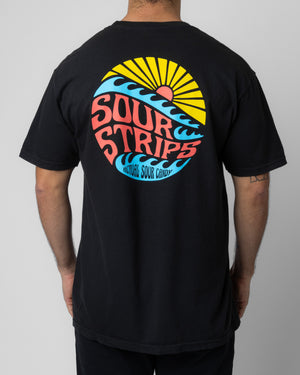 A person is shown from the back, wearing an oversized Dawn Tee by SourStrips, featuring a colorful graphic design. The unisex design displays a sun, waves, and the text "SOUR STRIPS" in bold letters, along with the phrase "Actual Sour Candy." The shirt's design incorporates yellow, blue, red, and white colors.