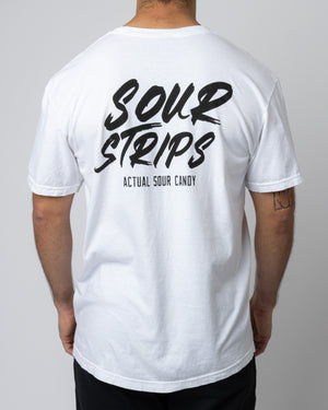 A person is standing with their back facing the camera, wearing an oversized box fit "Logo Tee - White" from SourStrips. The t-shirt features the text "Sour Strips" in bold, black letters and "ACTUAL SOUR CANDY" in smaller, capital letters underneath.