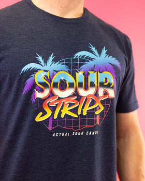 A person wearing the Miami Vice Tee from SourStrips, featuring a relaxed fit and a dark blue color. The t-shirt showcases a vibrant graphic design with palm trees and a sunset, accompanied by the words "Sour Strips" in large, bold letters above "Actual Sour Candy" in smaller text, all set against a bright pink background.