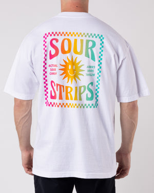 A person wearing the Good Times Tee White from SourStrips displays a colorful graphic on the back. This unisex design features a stylized sun, the words "Sour Strips" in bold, and text that reads "Actual Sour Candy." The vibrant design includes a gradient of pink, yellow, and green colors on this graphic T-shirt.